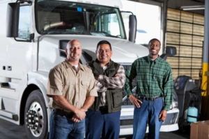 A group of fleet drivers gather, smiling, in front of a semi truck.