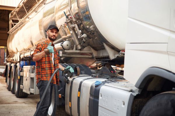 Truck driver gives a thumb’s up while fueling his semitruck after using a fuel card.