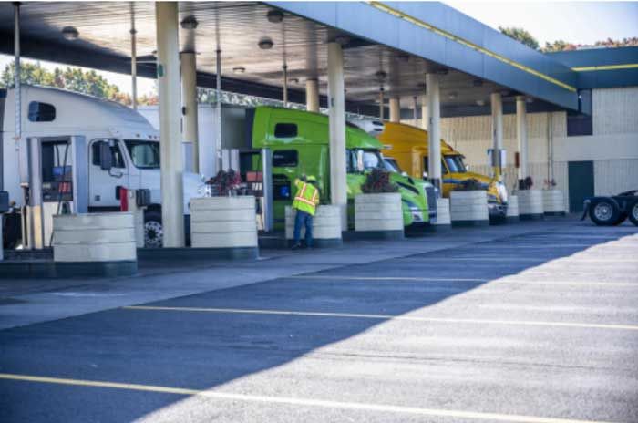 View of a bay of fueling stations where several semi trucks and their drivers are stopped to refuel.