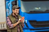 A happy truck driver uses his fleet fuel card app on his phone standing outside his rig.