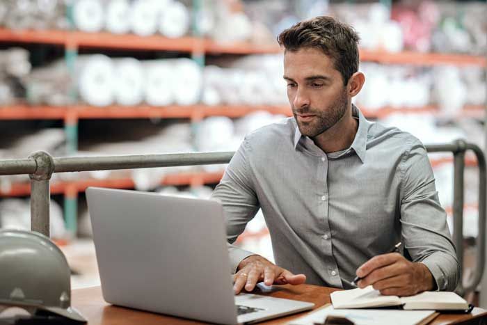 A business owner with fleets reviews fuel card usage in real-time from his laptop in a warehouse.