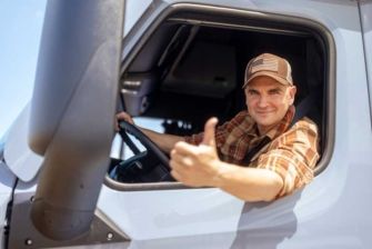 A happy truck driver gives a thumb’s up while leaning outside his fleet window.